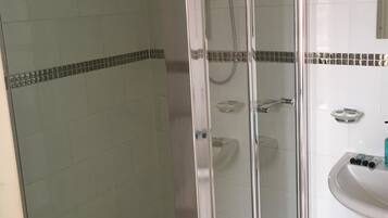Eine Duschkabine mit Glas, eine weiße Fliesenwand und ein kleines Waschbecken mit Pflegeprodukten.