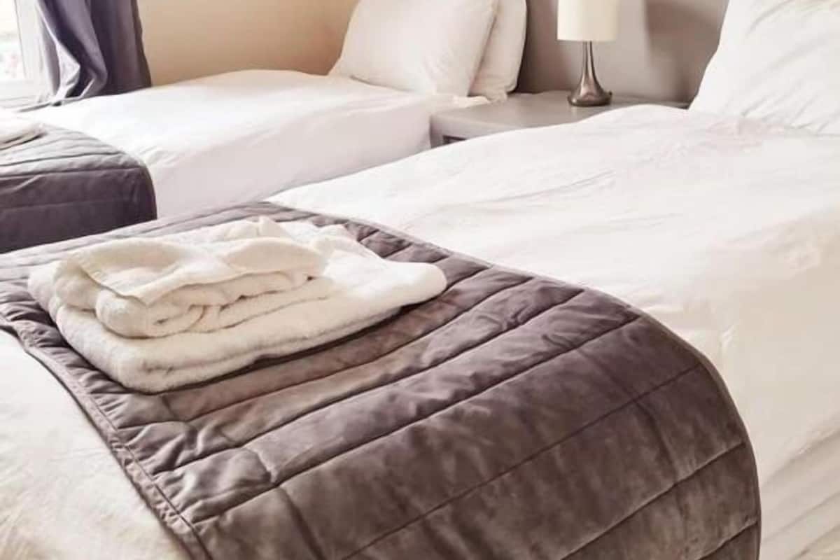 A hotel room with two beds, a headboard, a nightstand with a lamp, and a painting on the wall.