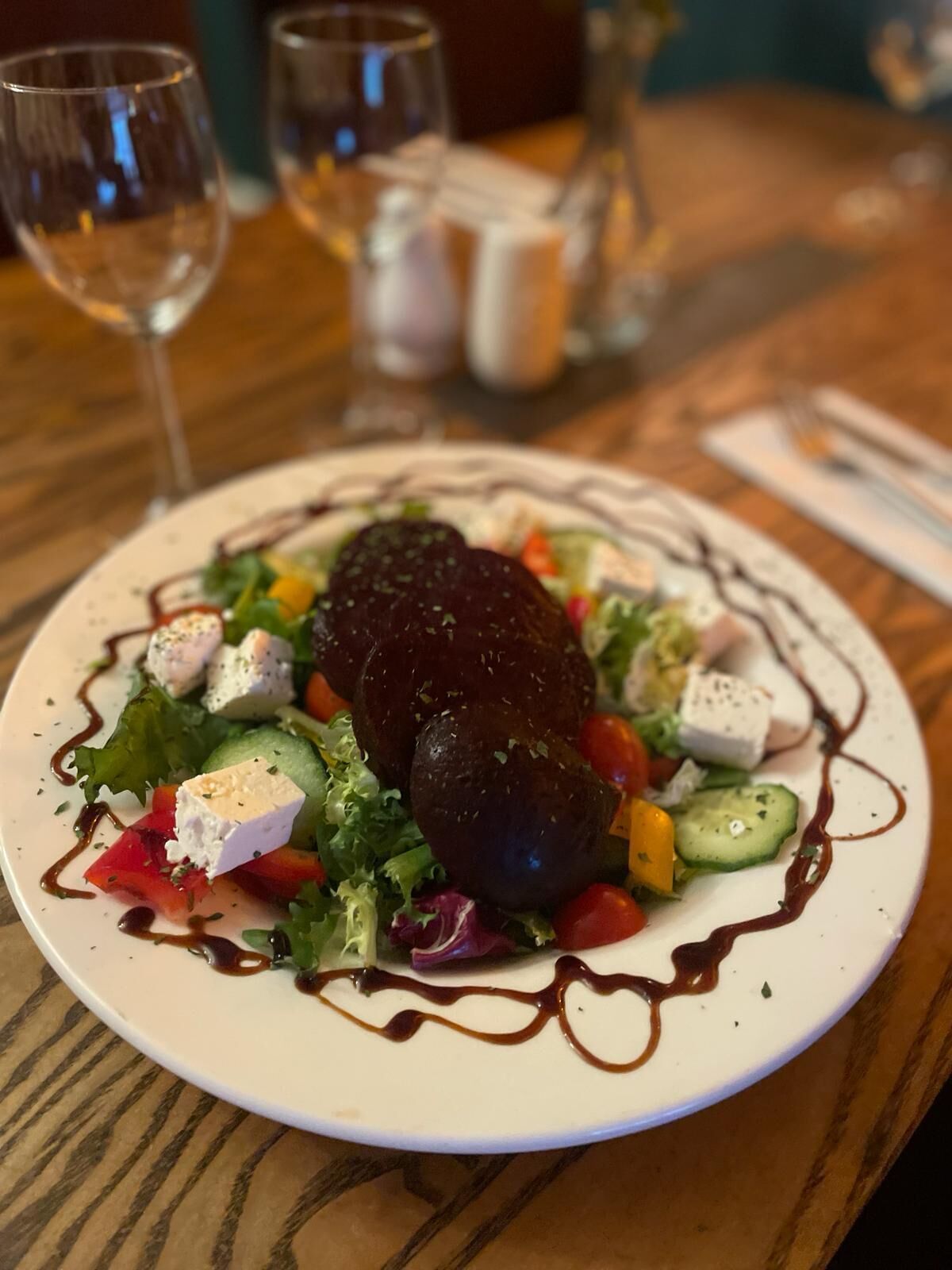 A plate of food with a dark-colored meat centerpiece, surrounded by vegetables and cheese, on a white plate with a brown sauce drizzle.