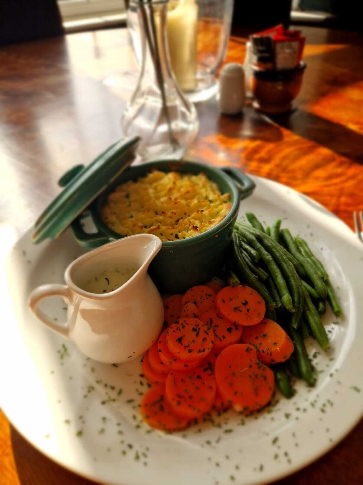 Une assiette contenant un plat de riz jaune, des haricots verts et des carottes en tranches, accompagné d’un petit pichet blanc.