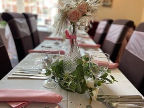 A dining table set with a clear glass bottle, white roses, and green foliage.