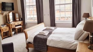 Una habitación de hotel con cama, escritorio, silla, televisión y ventana con cortinas.