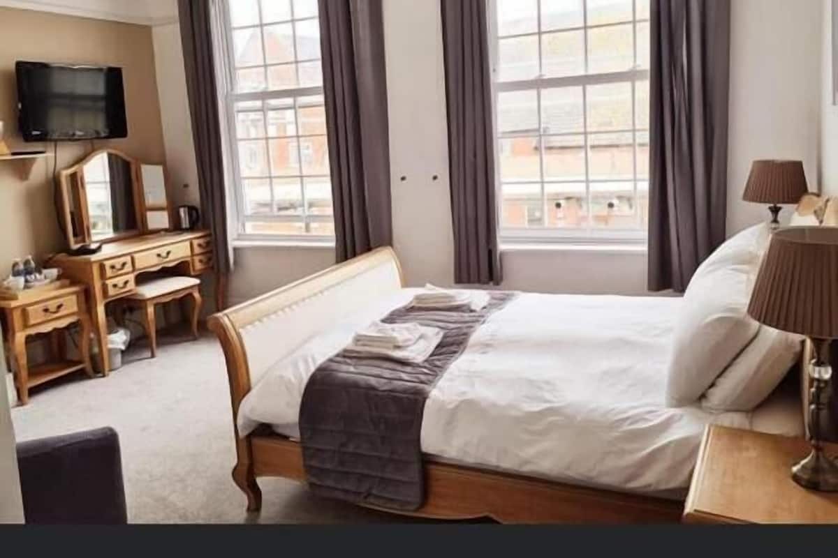 A hotel room with a bed, a desk, a chair, a TV, and a window with curtains.