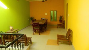 A dining area with a table and chairs, a ceiling fan, and a staircase with a railing. - Hotel Satkar (Jaipur)