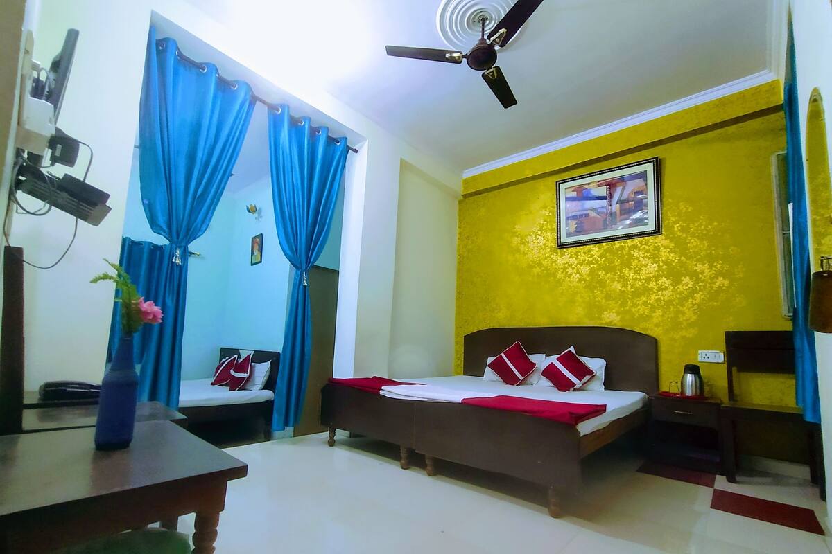 A hotel room with a bed, a desk, a chair, a ceiling fan, and a window with blue curtains.