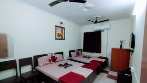 A bedroom with two beds, a ceiling fan, an air conditioning unit, a TV, and a wooden wardrobe. - Hotel Satkar (Jaipur)