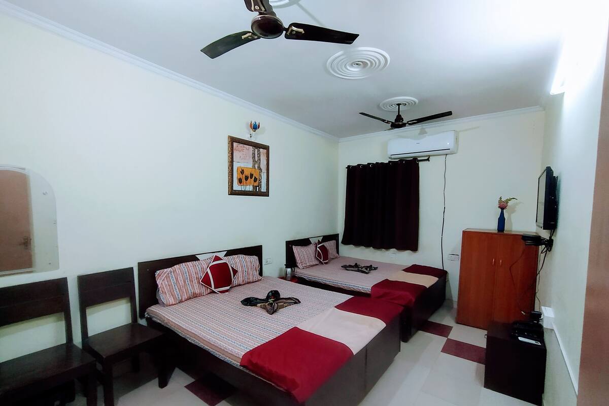 A bedroom with two beds, a ceiling fan, an air conditioning unit, a TV, and a wooden wardrobe.