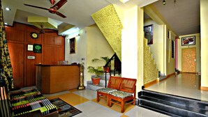 A reception area with a wooden desk, a clock, a bench, and a staircase leading to another floor. - Hotel Satkar (Jaipur)
