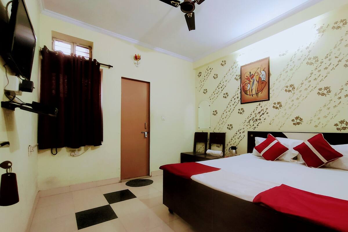 A hotel room with a bed, a television, a door, and a wall with floral wallpaper.