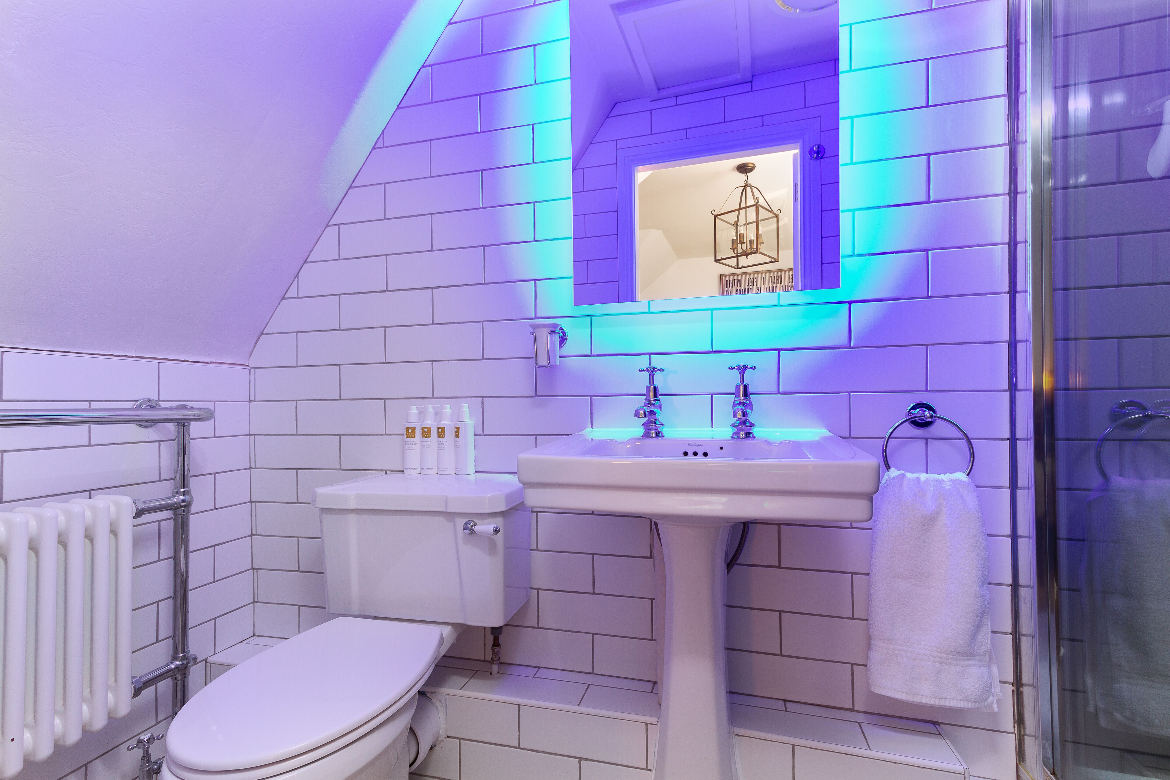 A bathroom with white tiles, a white toilet, a pedestal sink, and a glass shower enclosure.
