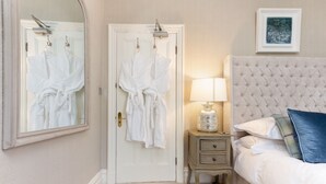 A bedroom with a bed, a nightstand, a lamp, a mirror, and two white robes hanging on a door. - Glencree (Windermere)