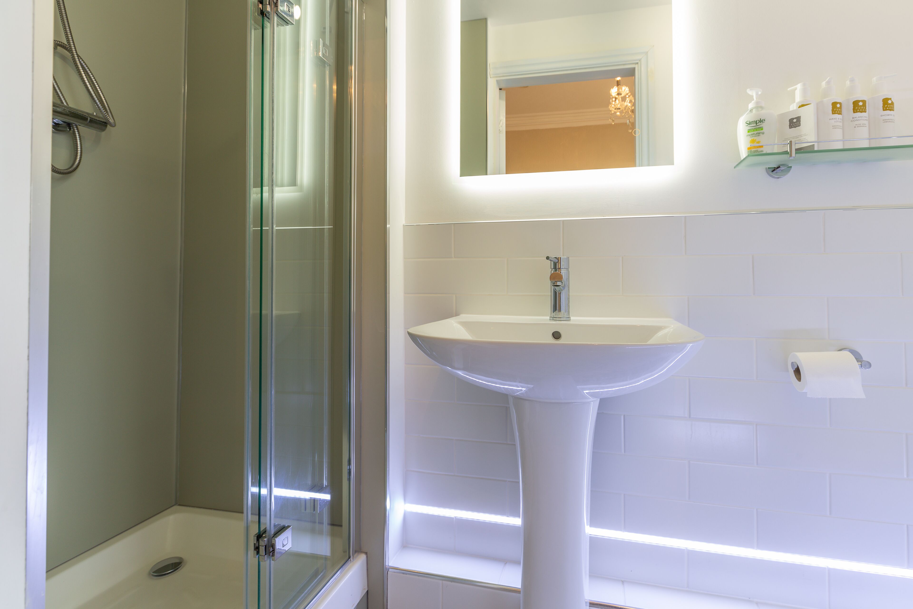 A bathroom with a glass shower enclosure, a pedestal sink, and a mirror above the sink.