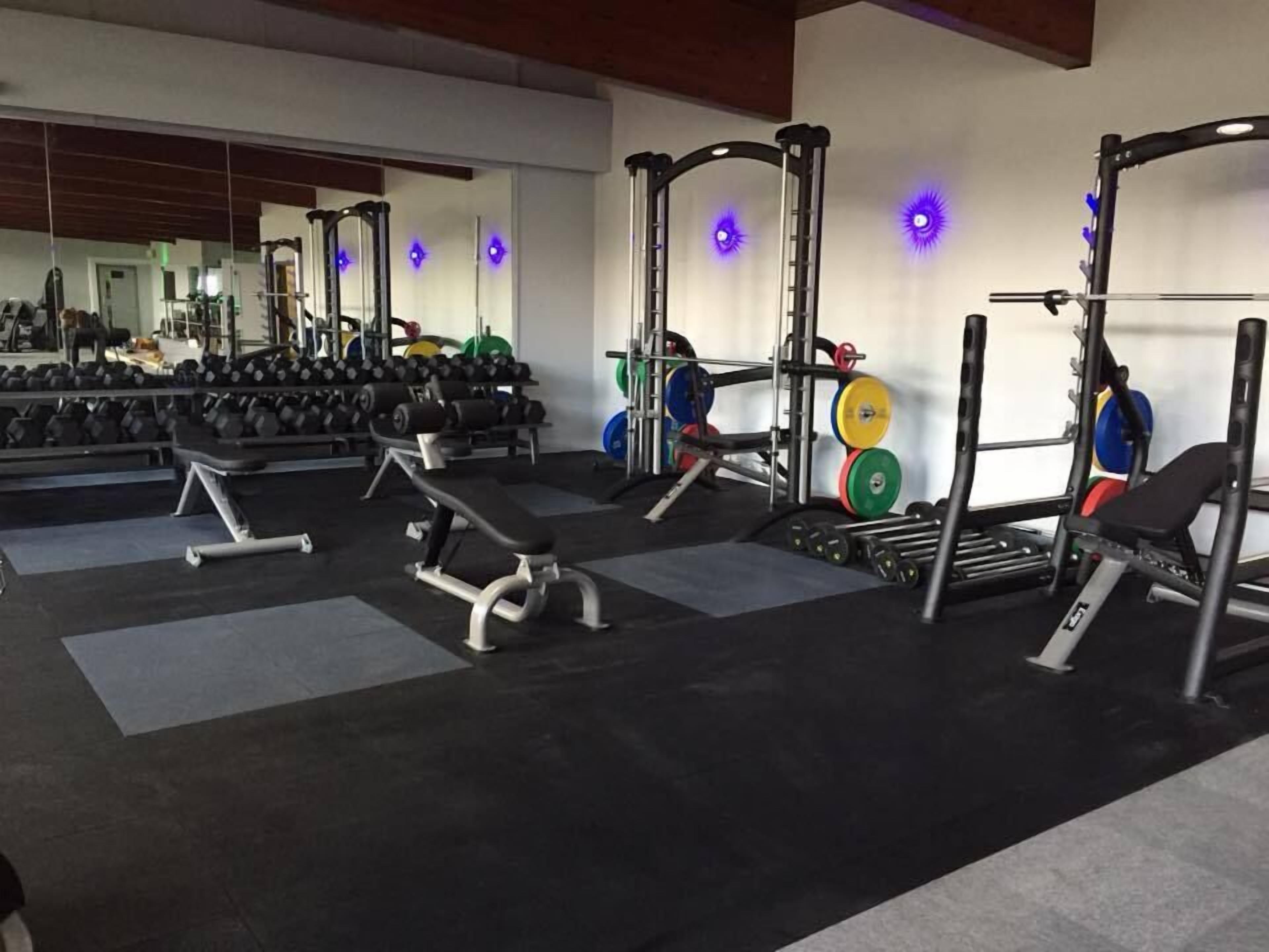 A gym with weightlifting equipment, benches, and dumbbells.