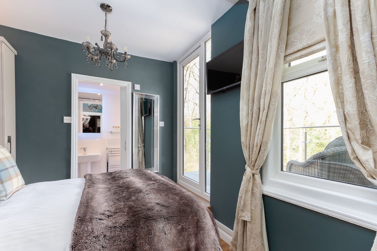 A bedroom with a large bed, a chandelier, and a view of the outside through a window with curtains.