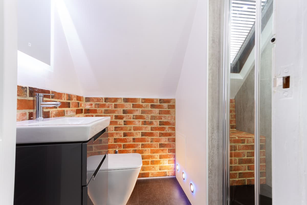 A modern bathroom with a white sink, black cabinet, and a toilet against a brick wall.