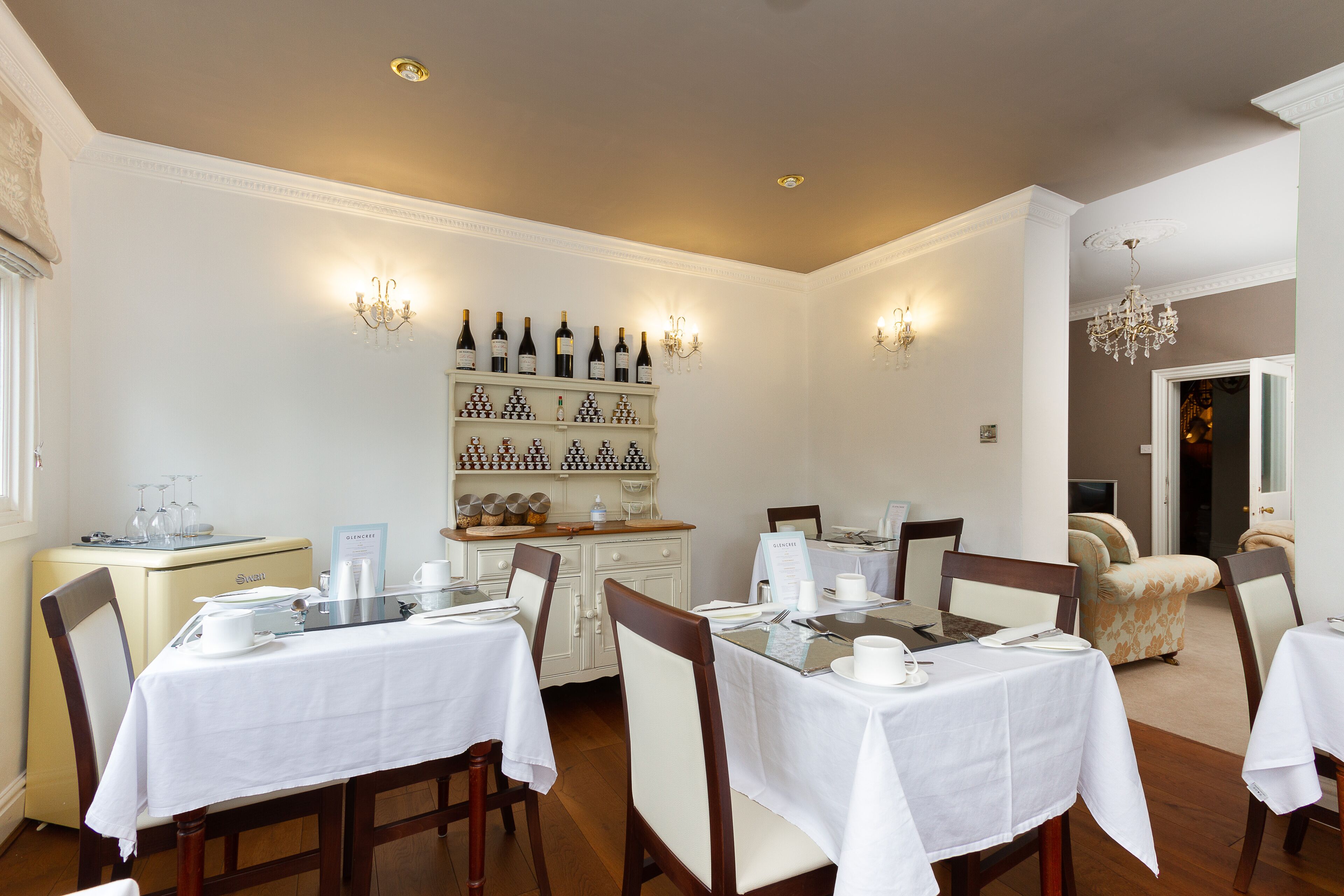 Un comedor con mesas dispuestas para el servicio, una vitrina de vinos y un rincón de estar acogedor.