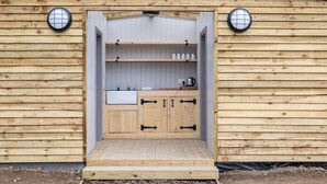 A wooden structure with a built-in kitchen featuring a sink, cabinets, and shelves. - Three Tuns (Helston)