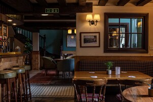 Un acogedor interior de restaurante con taburetes de madera, una mesa de madera con una planta en maceta y un ventanal con vistas al exterior.