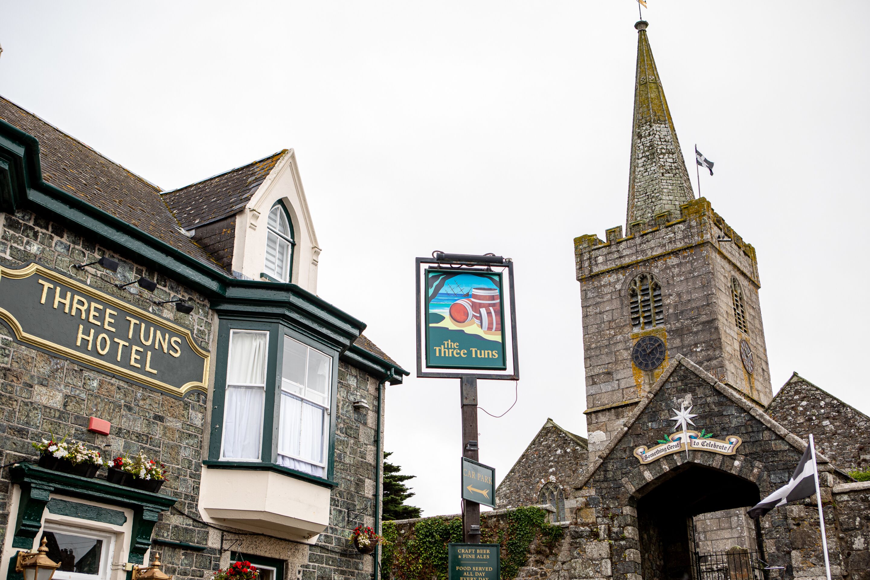 Un edificio histórico con un cartel del Hotel Three Tuns y una iglesia con campanario.