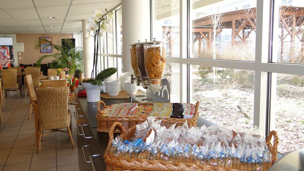 A buffet area with wicker chairs, a large window, and a food dispenser. - All Suites Appart Hôtel | Bordeaux - Mérignac Aéroport (Merignac)