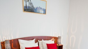 A neatly made bed with white and red pillows, a wooden headboard, and a cityscape painting above it. - All Suites Appart Hôtel | Bordeaux - Mérignac Aéroport (Merignac)