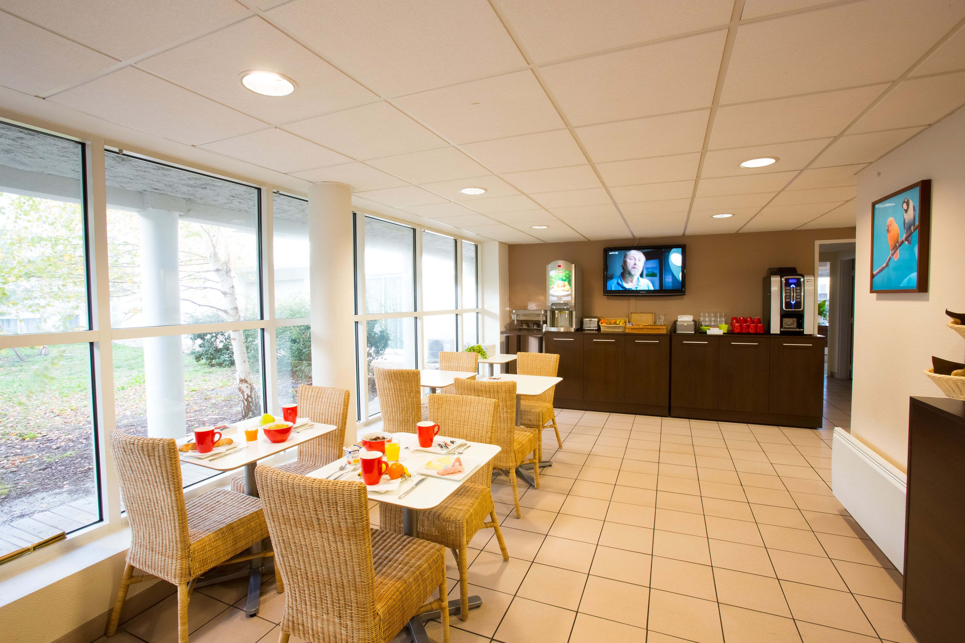 A dining area with wicker chairs and tables, a kitchen counter, and a television screen.