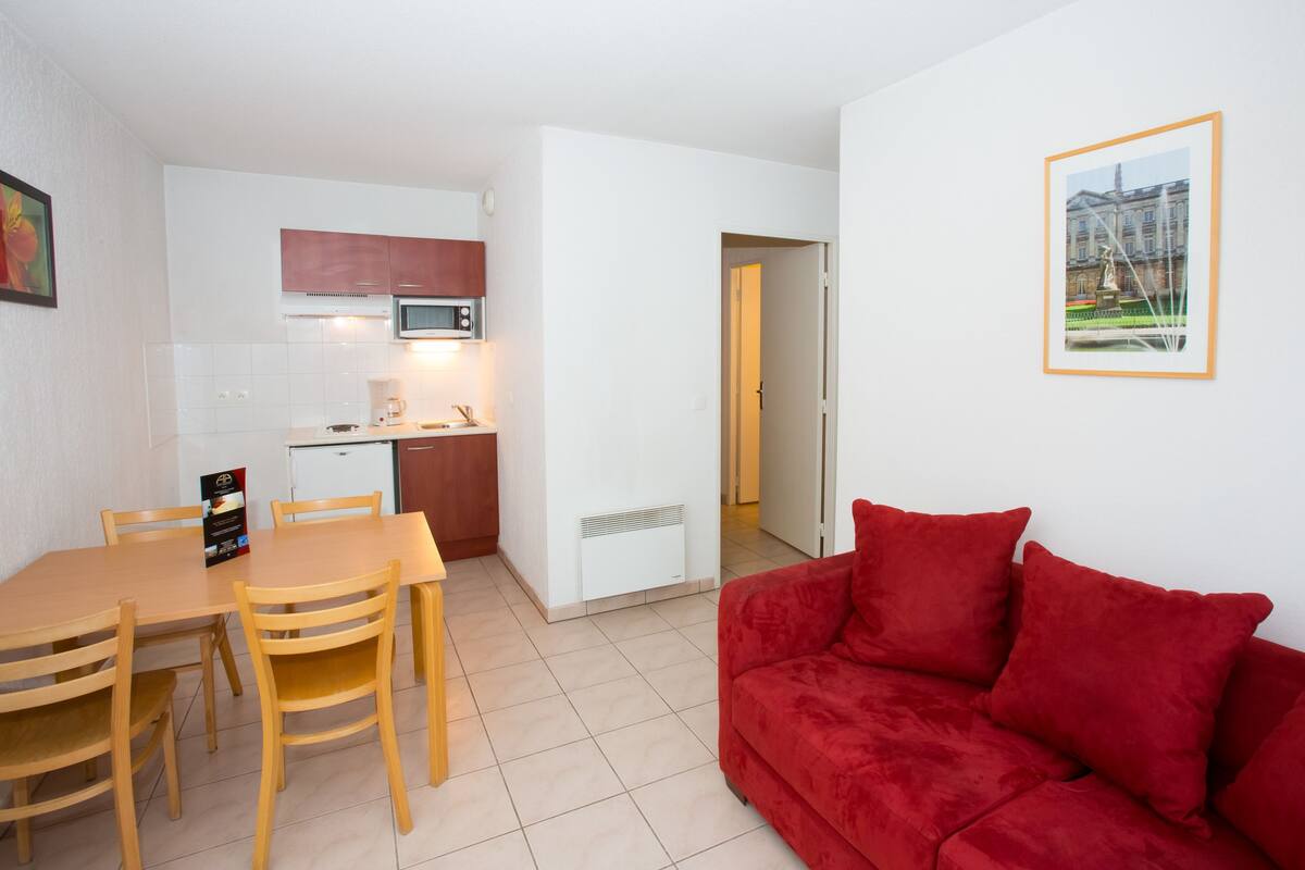 A compact living space with a kitchenette, a dining area, and a red sofa.