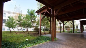 An outdoor wooden deck area with a covered section, surrounded by greenery and trees. - All Suites Appart Hôtel | Bordeaux - Mérignac Aéroport (Merignac)