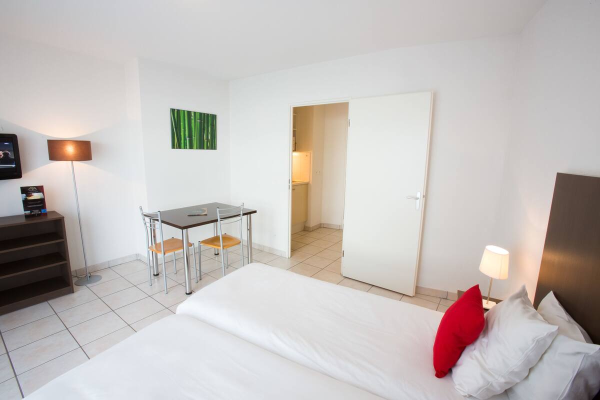 A hotel room with a bed, a desk, a chair, and a door leading to a bathroom.