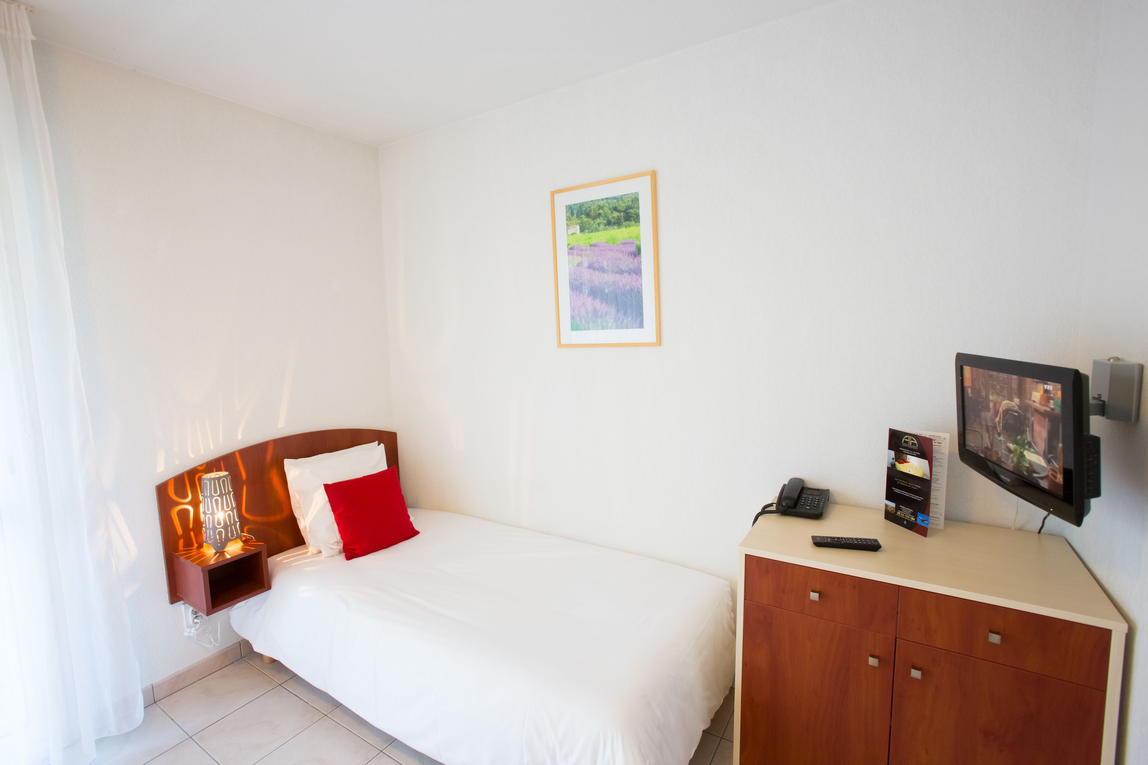 A hotel room with a bed, a nightstand with a lamp, a TV, and a wooden cabinet.