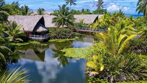 Un resort tropical con bungalós de techo de paja, un estanque con nenúfares y palmeras.
