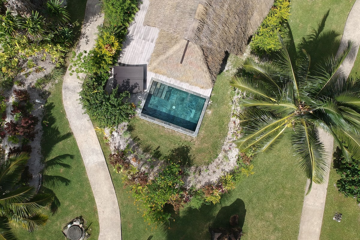 An aerial view of a resort with a swimming pool surrounded by palm trees and various tropical plants.