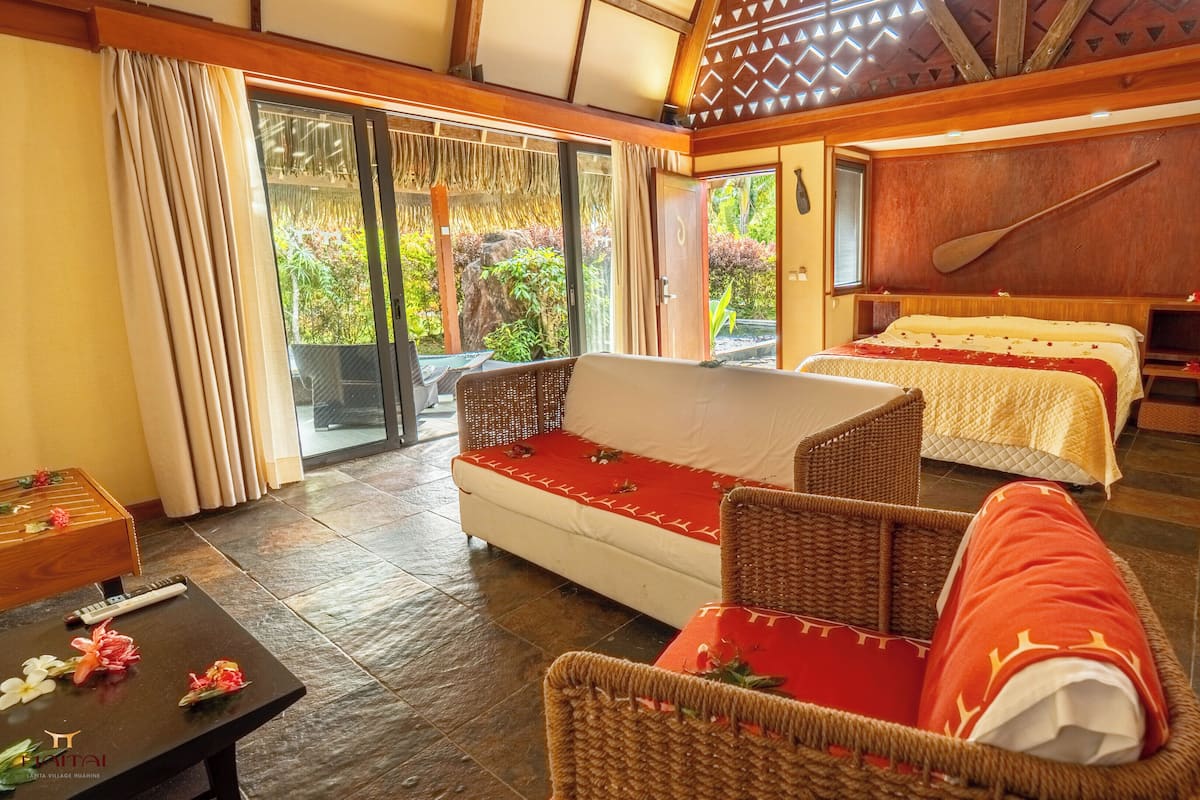 A hotel room with a sofa, two beds, a wooden paddle, and a view of greenery.