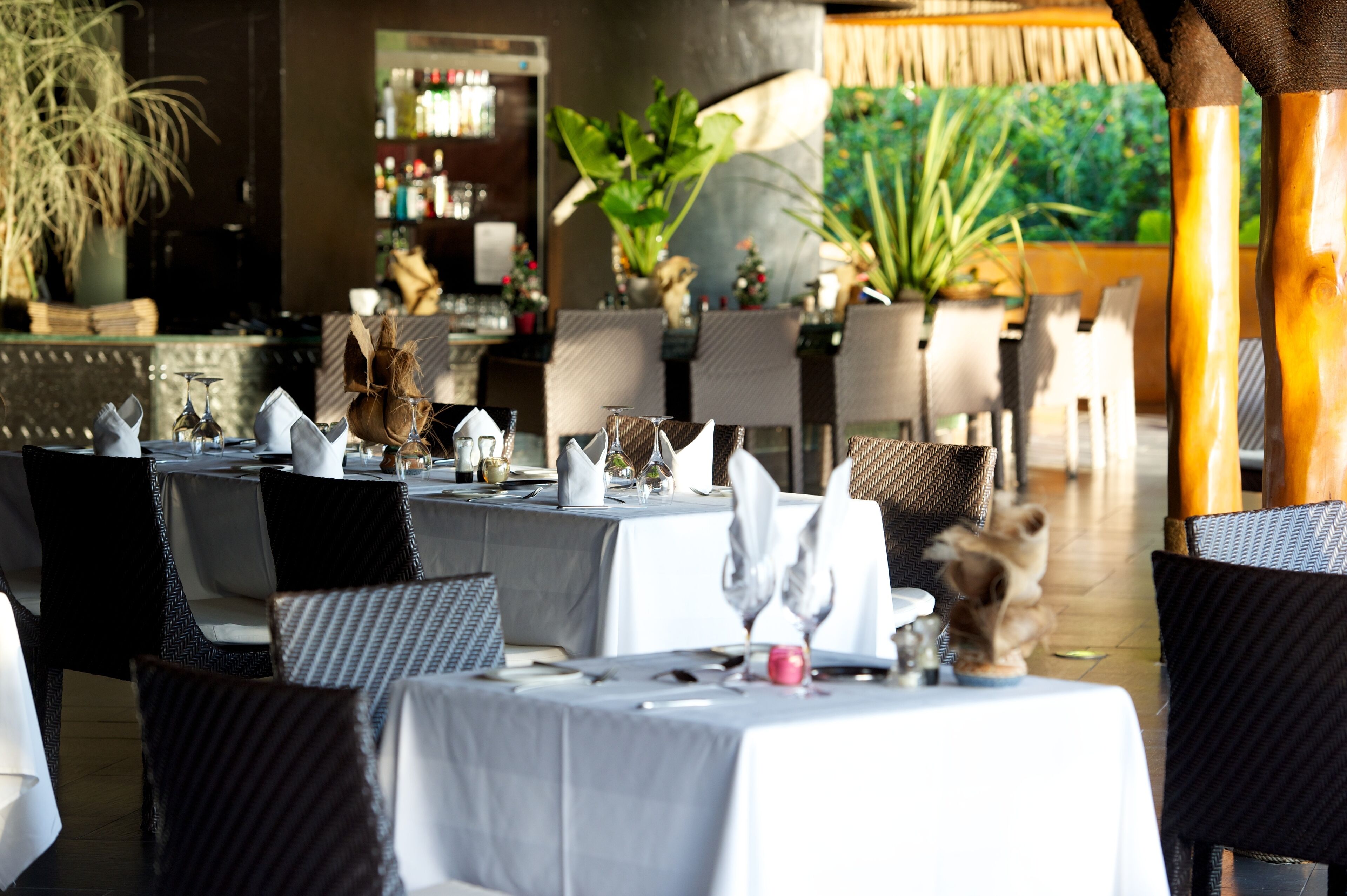 A restaurant with tables set for dining, chairs, and potted plants.