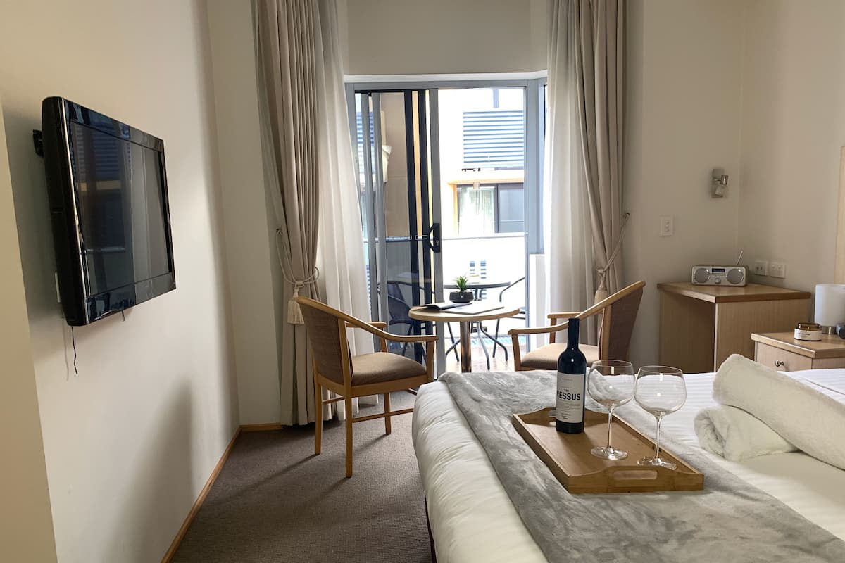 Quarto de hotel com cama, televisão, mesa de jantar com cadeiras, pequena cozinha e varanda com cortinas.