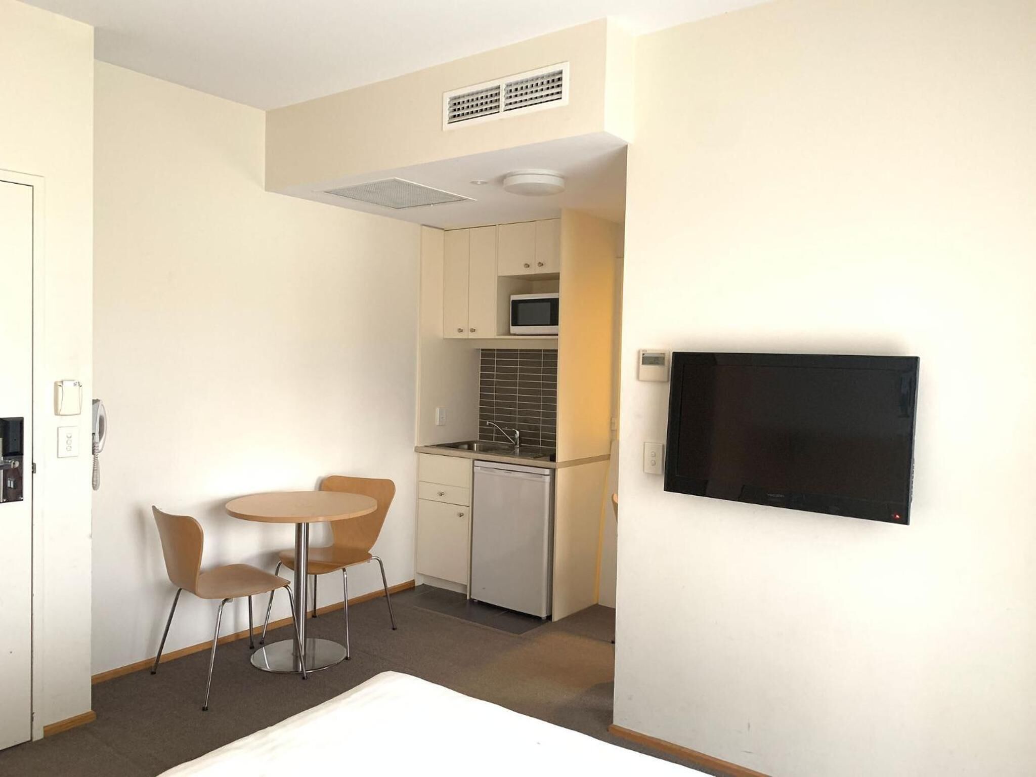 Cocina compacta con microondas, fregadero y lavavajillas. Cuenta con un pequeño comedor con una mesa y dos sillas. Un televisor de pantalla plana está montado en la pared.