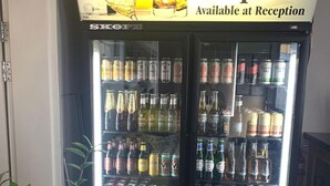 Un réfrigérateur à boissons contenant une variété de boissons, notamment du vin, de la bière et des spiritueux, avec une pancarte au-dessus indiquant : « Vin, bière et spiritueux disponibles à la réception ».