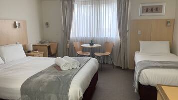 Habitación de hotel con dos camas, un escritorio, una silla, una mesita y una ventana con cortinas.