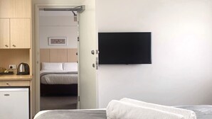 Une chambre d’hôtel avec un lit, un téléviseur fixé au mur, une petite kitchenette équipée d’une bouilloire et une porte donnant sur une autre pièce.