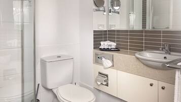 A modern bathroom with a toilet, a sink, a shower, and a mirror.