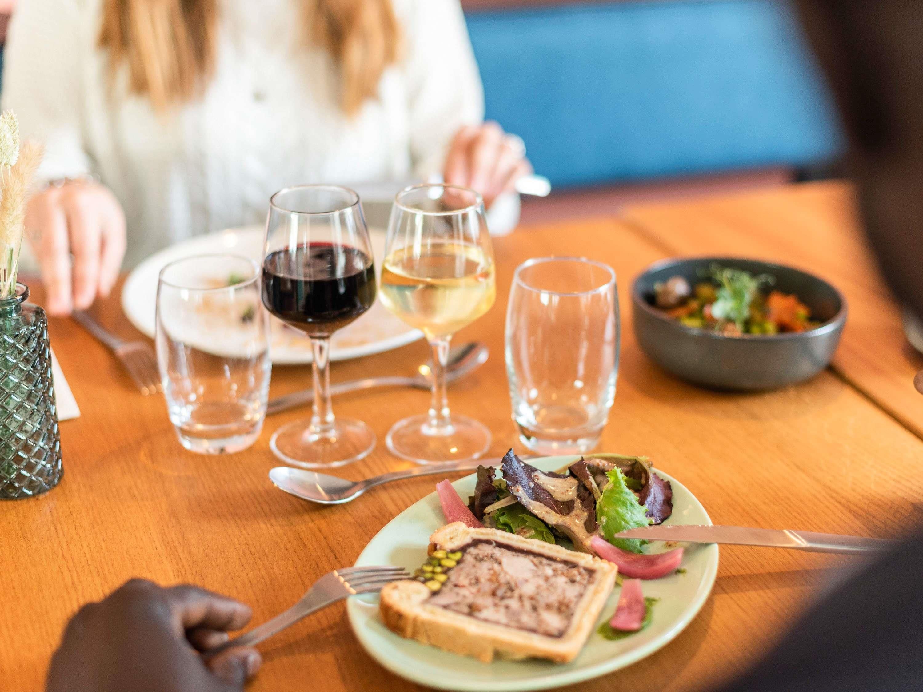 Una mesa de comedor con un plato de comida, copas de vino y un tazón de ensalada.