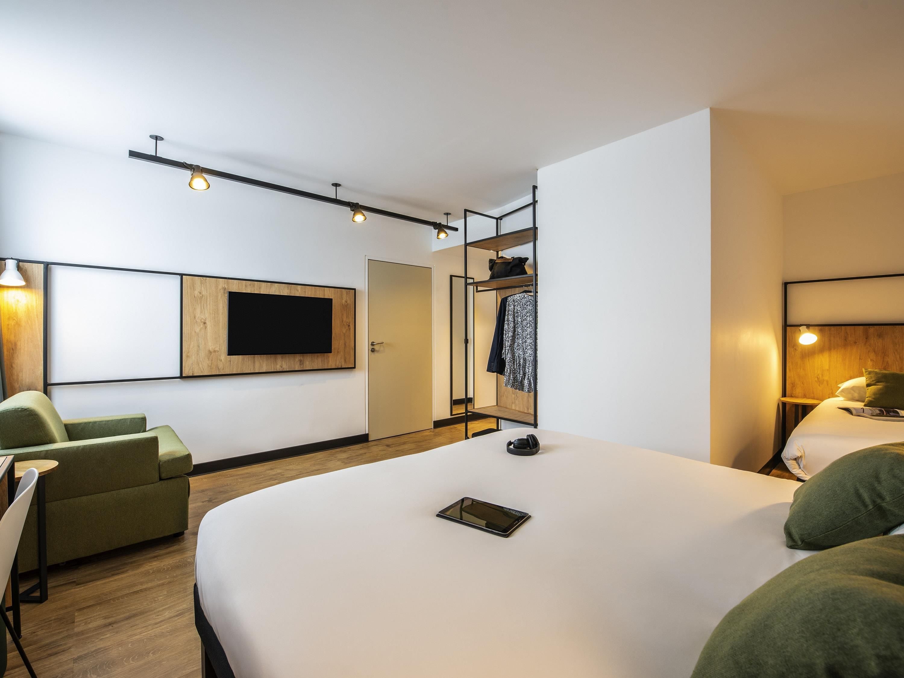 Een moderne hotelkamer met een groot bed, een zithoek met een bank en stoelen, een aan de muur bevestigde televisie en een garderobe met spiegel.