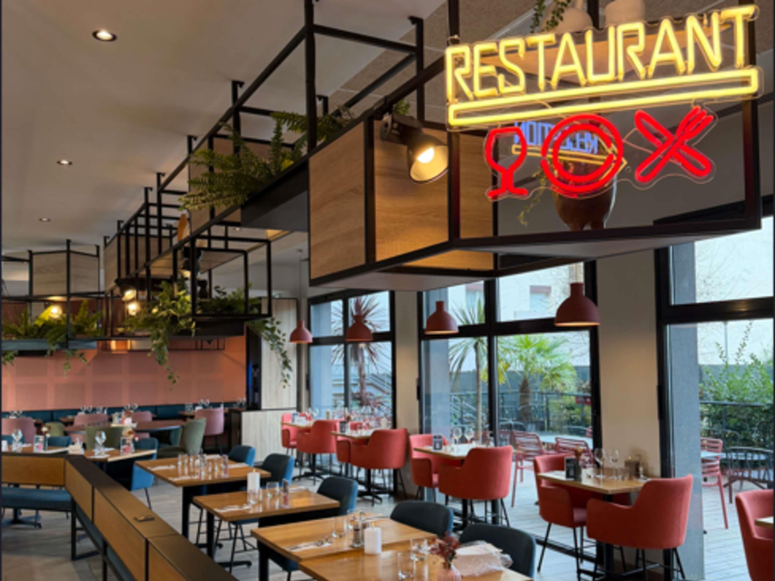 Ein Restaurantinneres mit einer Neonreklame, roten Stühlen und Tischen.