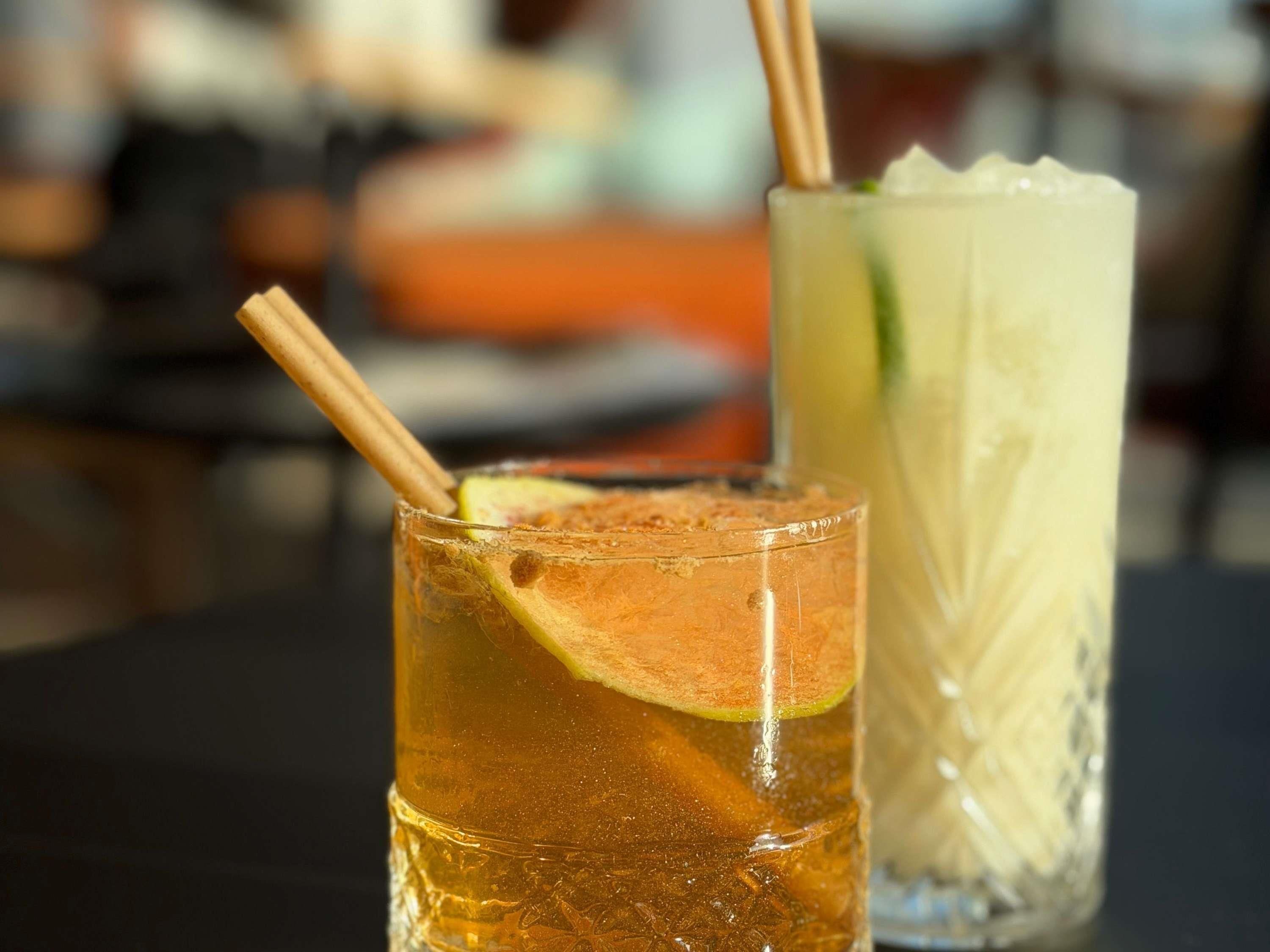 Two glasses of beverages with straws and a slice of lime, placed on a table.