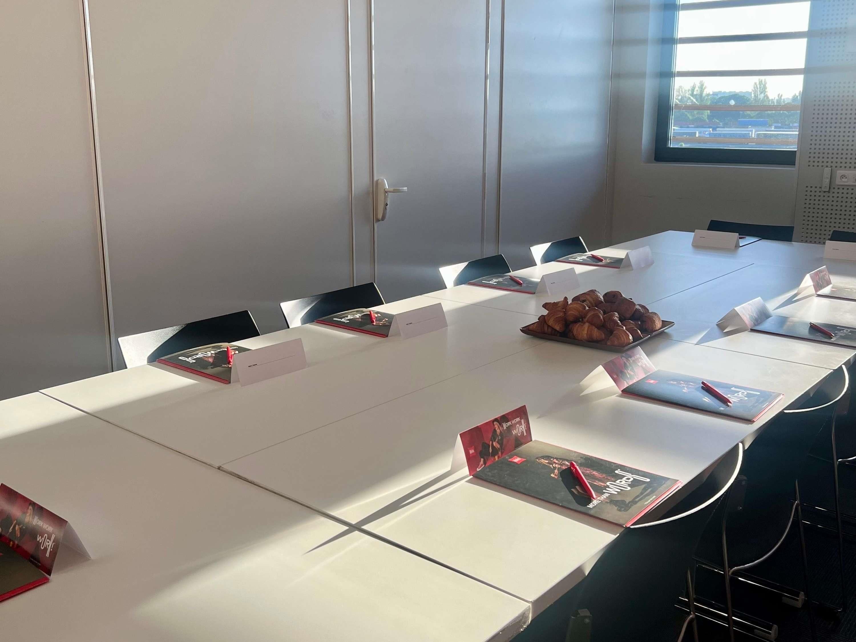 Una sala conferenze con un lungo tavolo, cartellini identificativi e un piatto di croissant.