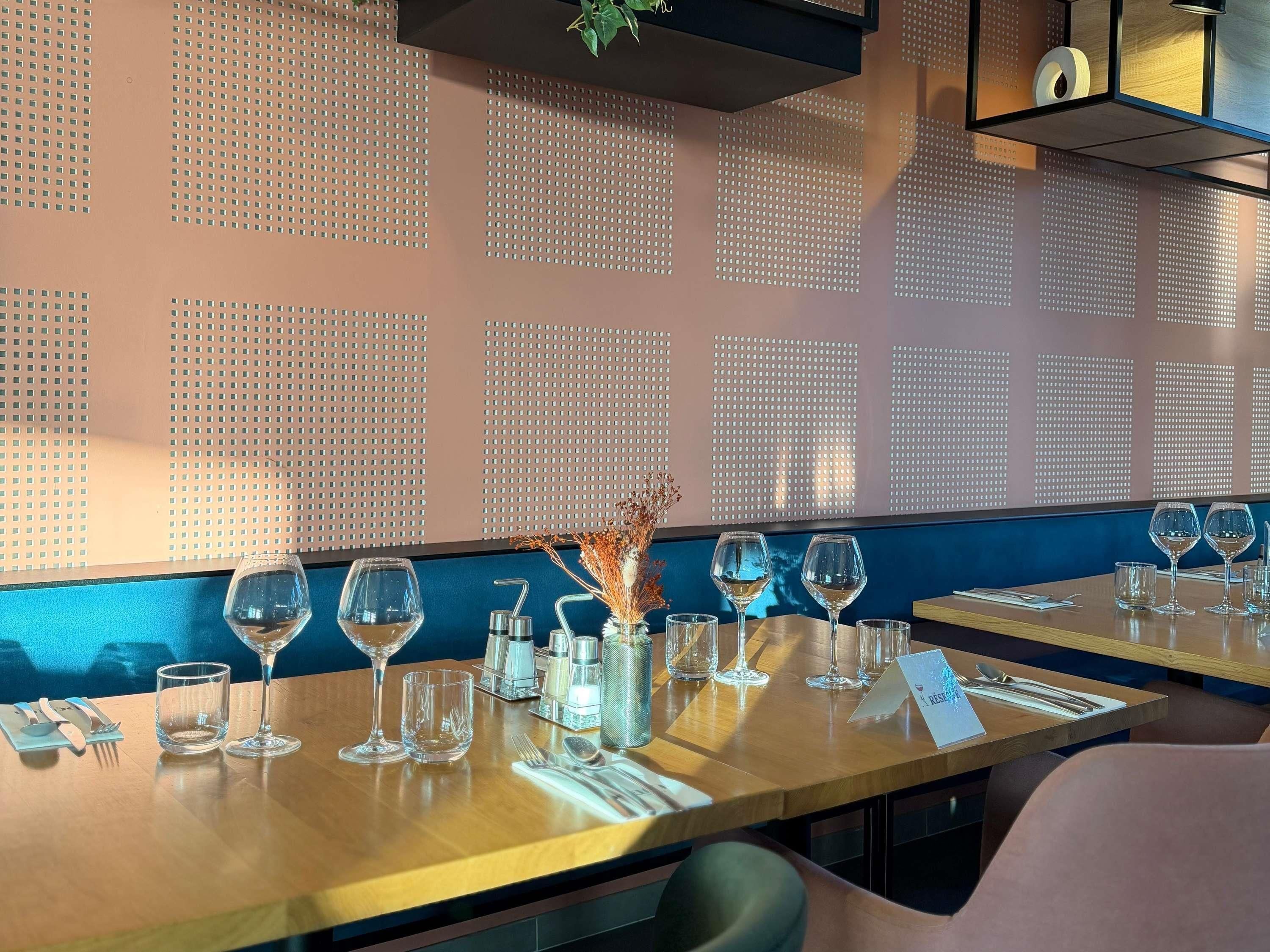 Interior de restaurante con mesas dispuestas para comer, un muro decorativo y una planta colgante.
