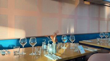 Interior de restaurante con mesas dispuestas para comer, un muro decorativo y una planta colgante.