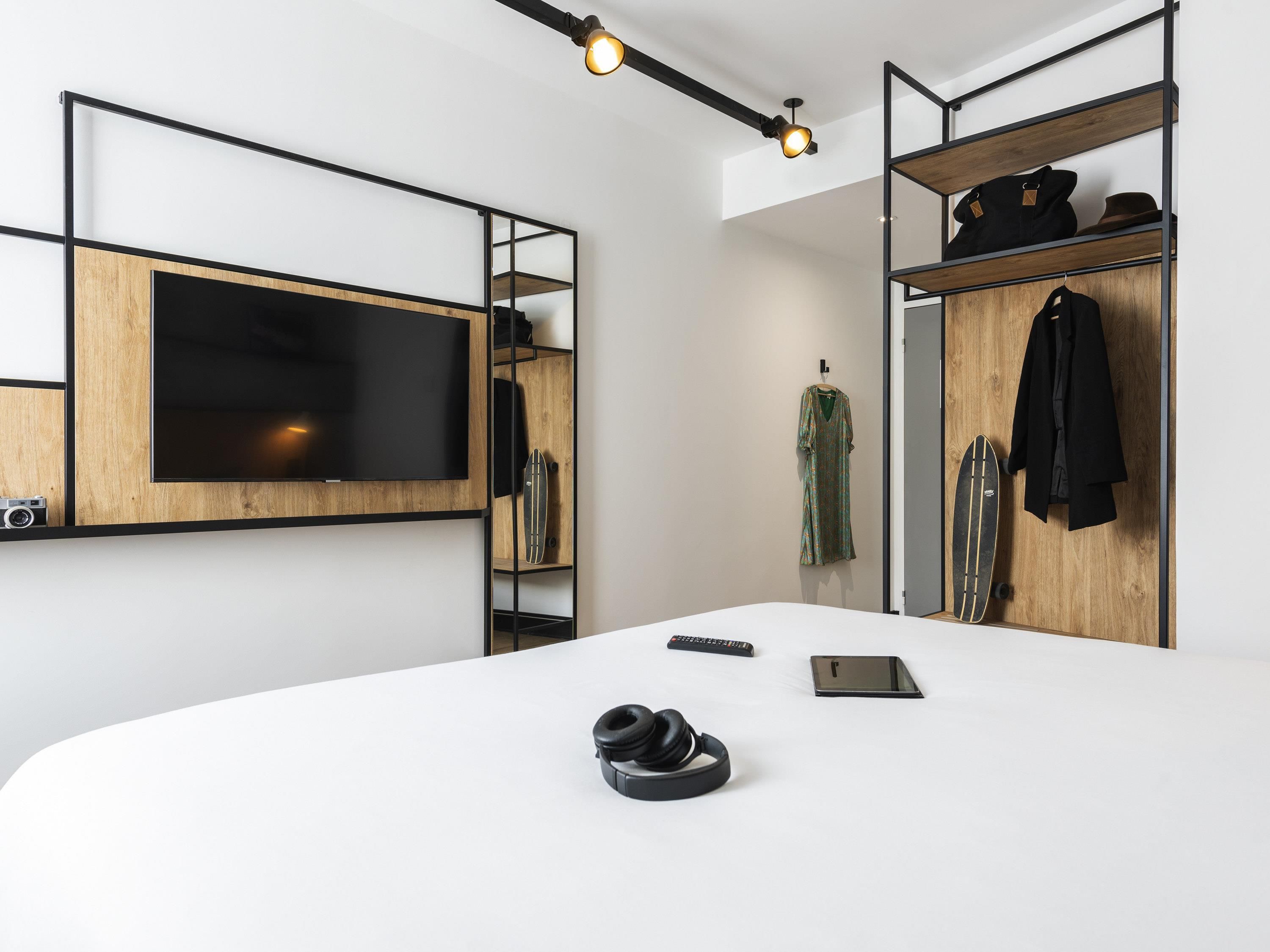 A modern room with a large flat-screen TV, a wooden wardrobe, and a white desk with headphones and a remote control.