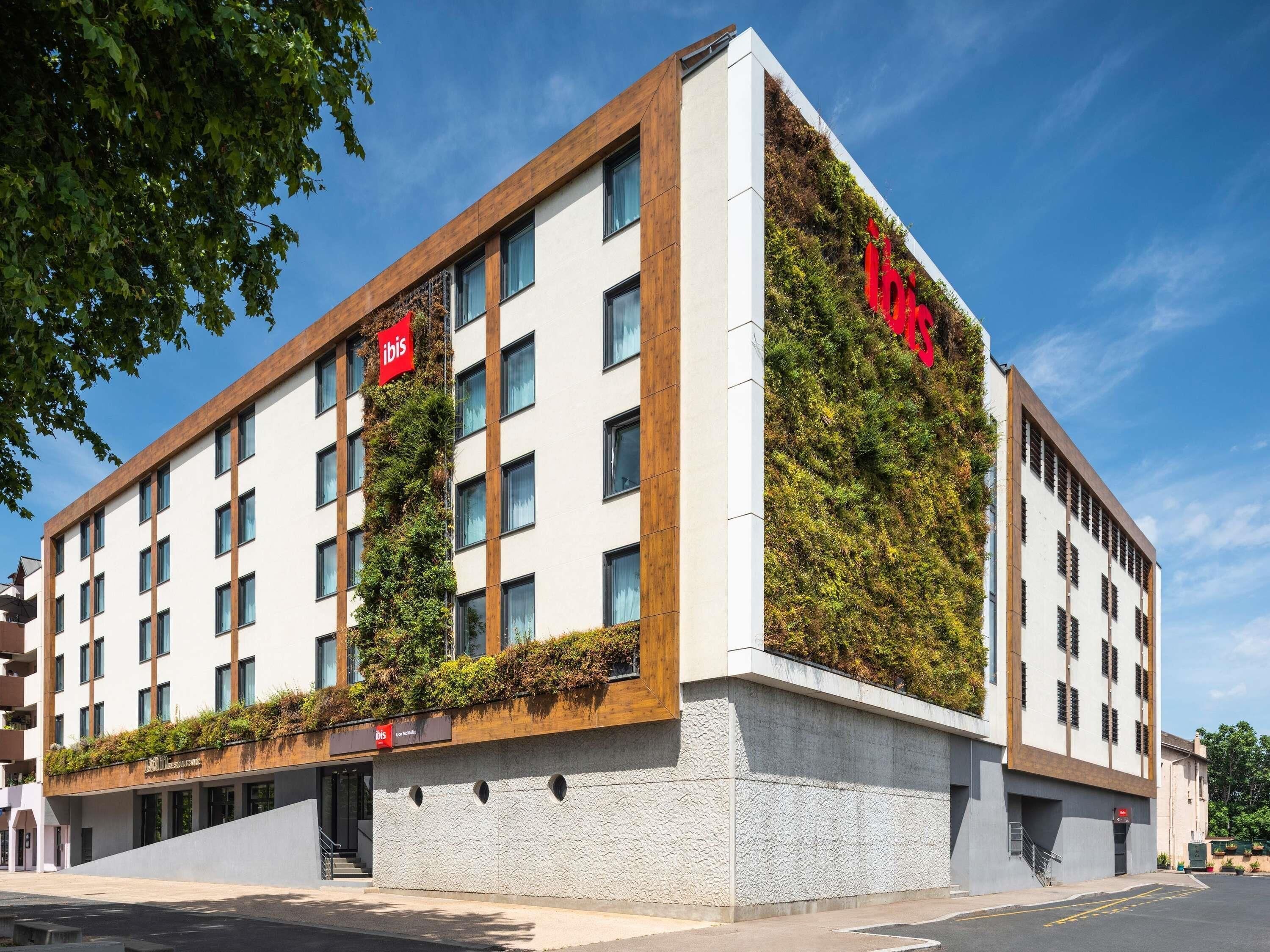 A modern hotel with a white facade, green vertical gardens, and red signage.