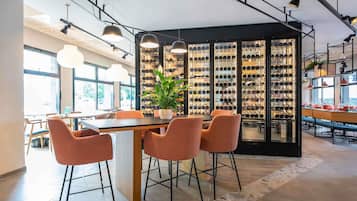 Un interno moderno con zona pranzo che include un tavolo in legno e sedie arancioni, una cantina con bottiglie e illuminazione a sospensione.